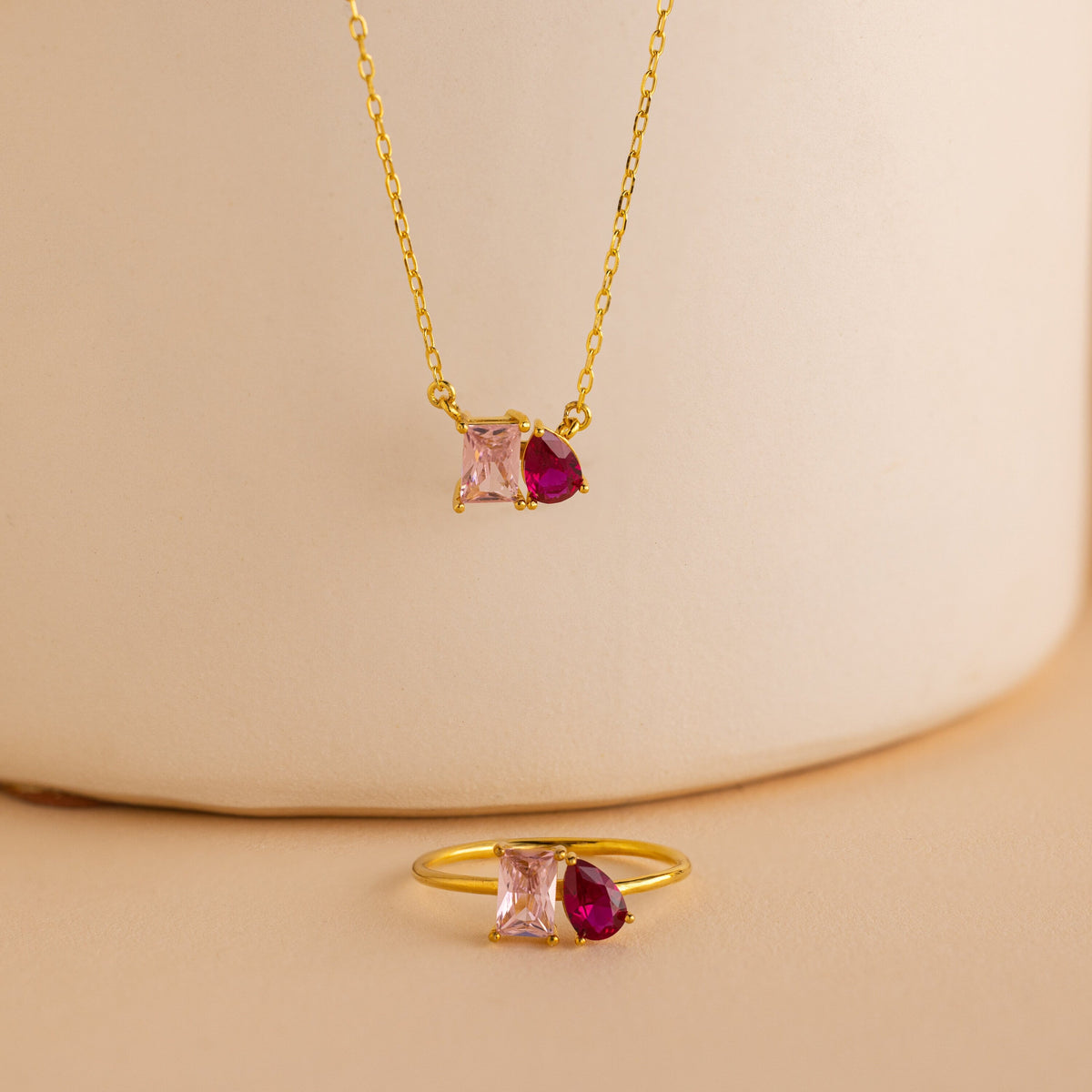 Toi et Moi Birthstone Necklace featuring pink square and red teardrop gemstones on a beige background—ideal for anyone seeking personalized gemstone or custom birthstone jewelry.