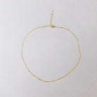 The Linden Chain by LLUME Jewelry is a delicate, dainty gold necklace with a fine, simple design, featuring an adjustable clasp and extender, crafted in 18K gold-plated finish and displayed on a light textured surface.
