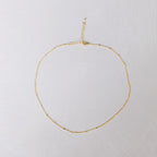 The Linden Chain by LLUME Jewelry is a delicate, dainty gold necklace with a fine, simple design, featuring an adjustable clasp and extender, crafted in 18K gold-plated finish and displayed on a light textured surface.