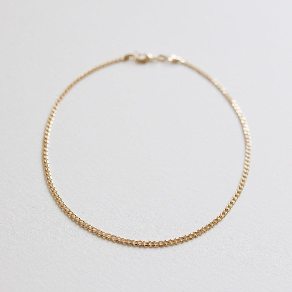 The Marie Chain by LLUME Jewelry is a delicate, thin gold bracelet with a small clasp, shown in a circle on a white background. Perfectly pairs with any 18k gold-filled necklace for an elegant, coordinated style.
