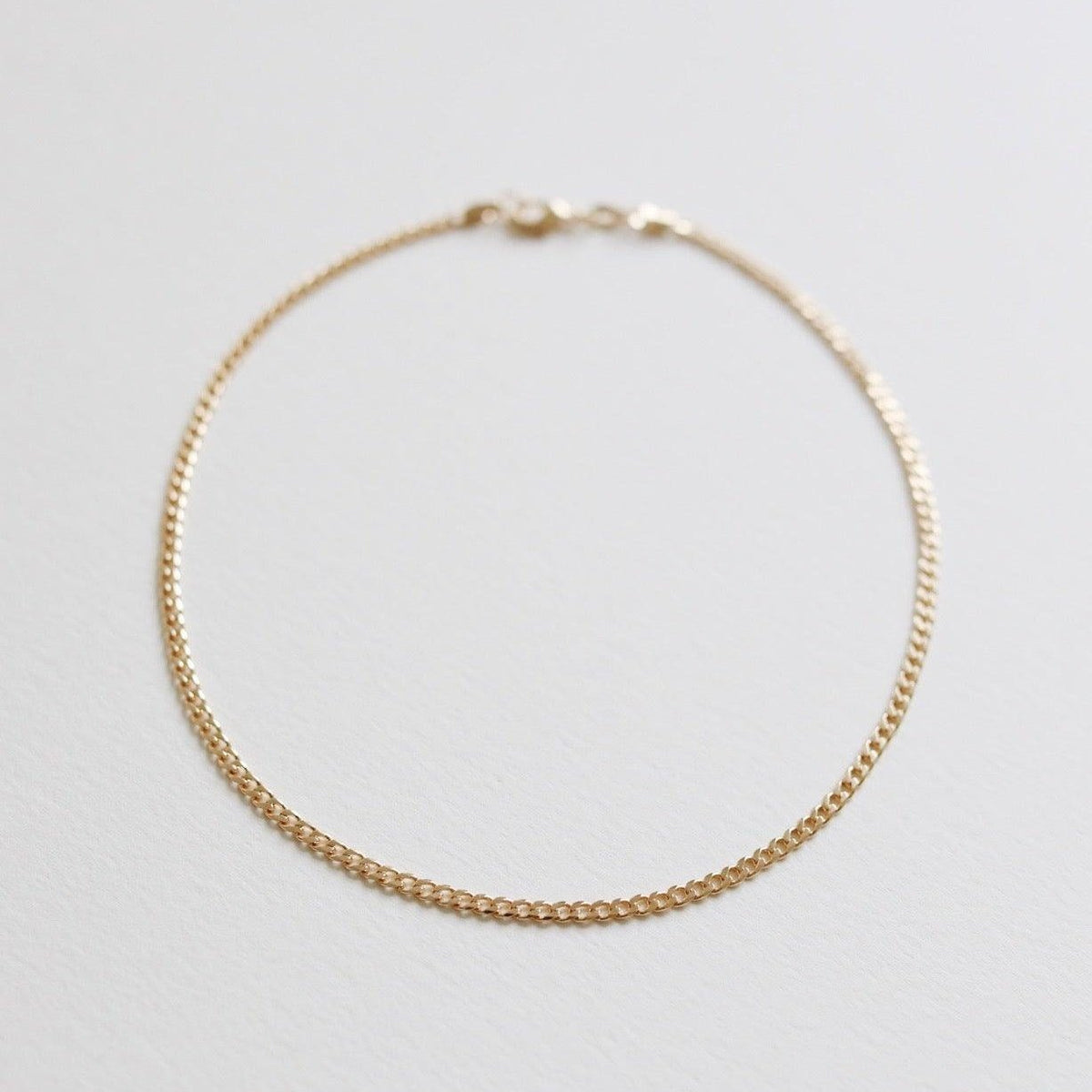 The Marie Chain by LLUME Jewelry is a delicate, thin gold bracelet with a small clasp, shown in a circle on a white background. Perfectly pairs with any 18k gold-filled necklace for an elegant, coordinated style.