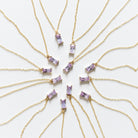 Ten Celia Necklaces by LLUME Jewelry, each a gold vermeil piece with a rectangular lilac gemstone pendant, are arranged in a circle on a white background, radiating outward like sunrays.