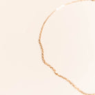 The Harlow Chain by LLUME Jewelry, an 18k gold filled necklace, is shown against a soft beige background, with its elegant link chain gently curving and slightly out of focus in the image.
