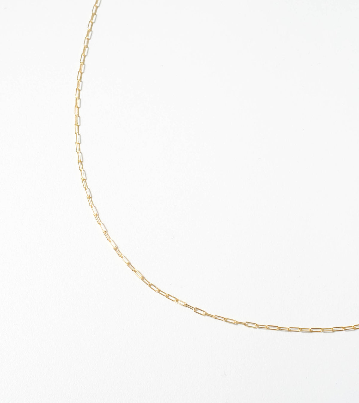 The Adelene Paperclip Chain by LLUME Jewelry, featuring small rectangular gold-plated links, is displayed in a graceful curve against a plain white background.