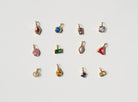 Twelve small, gold-plated charms by LLUME Jewelry are arranged in a row on white, perfect for creating your own Build a Birthstone Necklace.