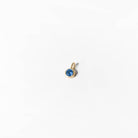 The Build a Birthstone Necklace by LLUME Jewelry features a small gold pendant with a round blue gemstone at the center, elegantly displayed against a plain white background.