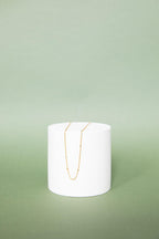 The Linden Chain by LLUME Jewelry, an 18K gold plated necklace, is displayed on a round white pedestal with a soft green backdrop—perfect for adding effortless elegance to any layered look.