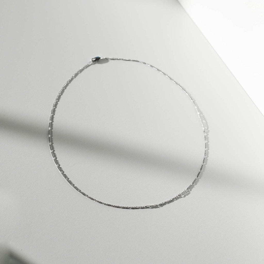 The Colette Necklace Silver by LLUME Jewelry, crafted from sterling silver, is arranged in an oval on a smooth, light surface with soft shadows—a versatile and elegant accessory.