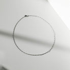 The Colette Necklace Silver by LLUME Jewelry, crafted from sterling silver, is arranged in an oval on a smooth, light surface with soft shadows—a versatile and elegant accessory.
