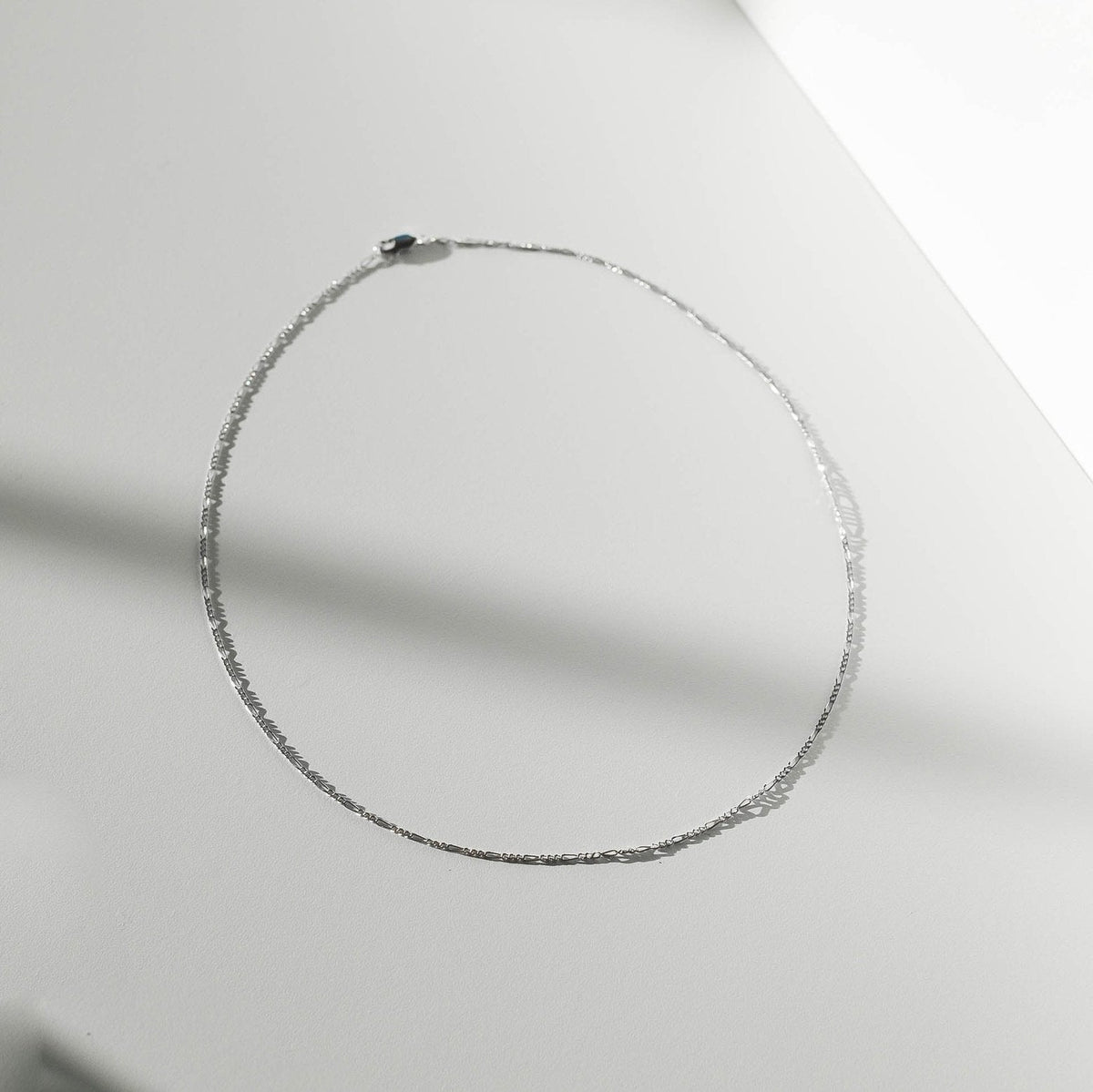 The Colette Necklace Silver by LLUME Jewelry, crafted from sterling silver, is arranged in an oval on a smooth, light surface with soft shadows—a versatile and elegant accessory.